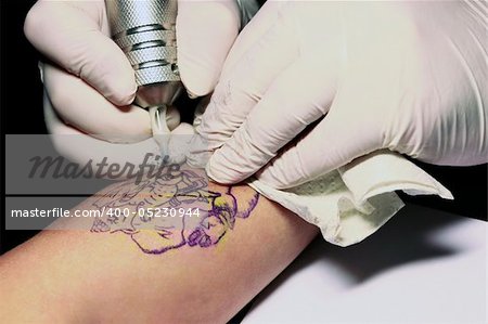 A tattoo artist applying his craft onto the hand of a female