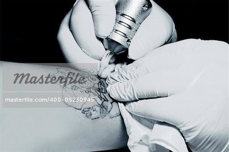 A tattoo artist applying his craft onto the hand of a female