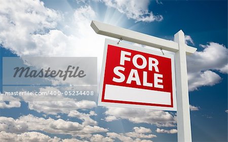 For Sale Real Estate Sign over Clouds and Blue Sky with Sun Rays.