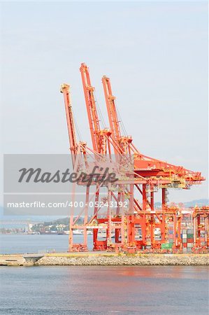 A vertical colour photograph of orange industrial cranes on the waterfront.