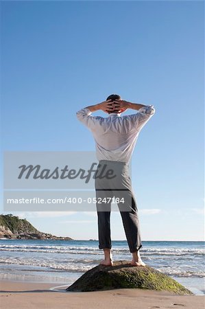 Businessman standing barefoot on a rock at the sea