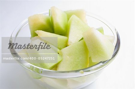 Melon honeydew pieces in a glass bowl on gradient background