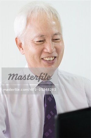 old asian business man smiling and using a laptop