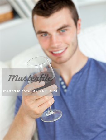 Charismatic young man holding a glass of wine sitting on a sofa in the living-room