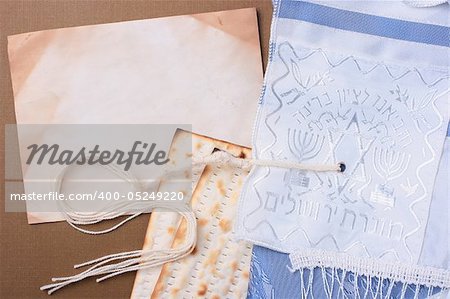 Matzah and a blue and white tallit laying next to an old piece of paper. Add your text to the paper.