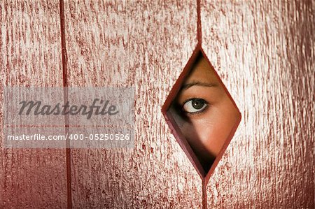 Woman peeks through a diamond shaped hole in a wall. Horizontal shot.