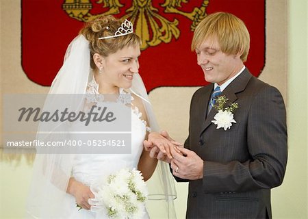 Happy newlyweds wear a wedding ring on the background of the national emblem.