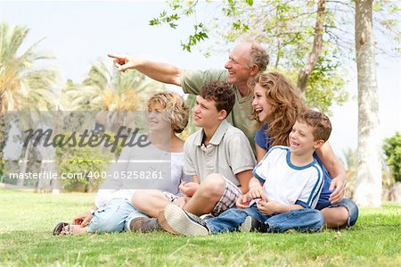potrait offamily sitting in a park and grandfather pointing with his finger