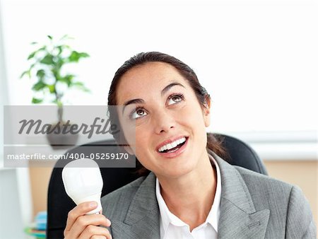 Surprised businesswoman holding a light bulb sitting in her office at her desk