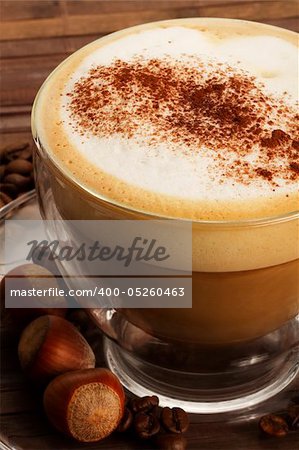 cappuccino with chocolate powder on milk froth and hazelnuts on wooden background