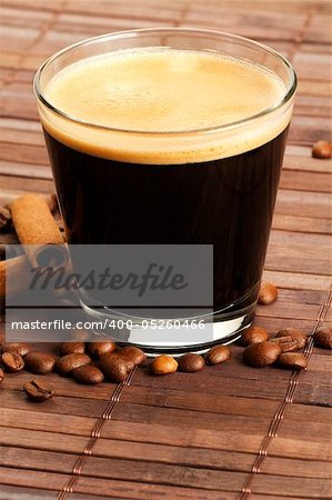 espresso in a short glass with coffee beans and cinnamon sticks from diagonal top on wooden background