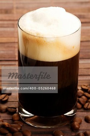 espresso with milk froth and coffee beans on wooden background