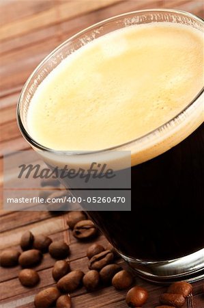 black espresso coffee in a short glass with coffee beans on wooden background