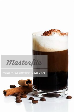 espresso in a straigt glass with milk froth cocoa powder, cinnamon sticks and coffee beans aside on white background