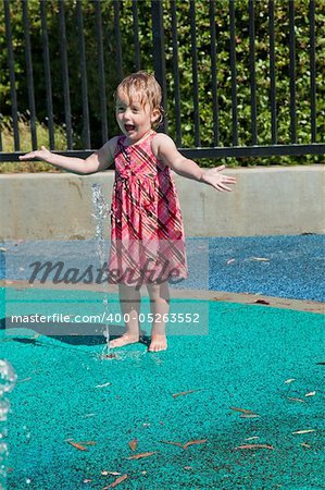 Cute little European toddler girl having fun with water at the playground in park