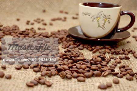 Coffee beans on focus and cup with cofee at background