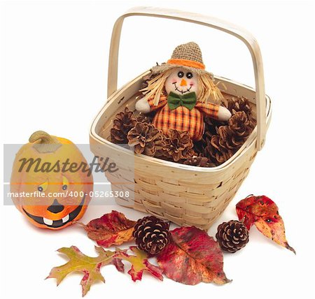 Various decorative Fall objects isolated on white: ceramic pumpkin, red leaves, and cones beside a basket of pine cones with scarecrow doll.
