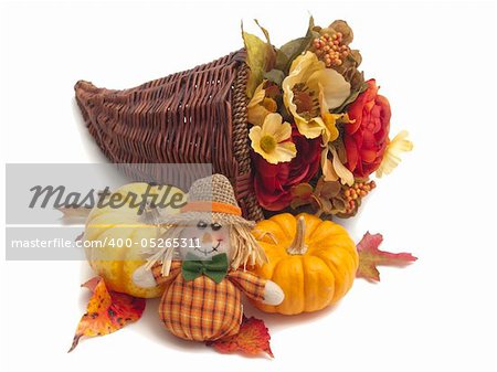 Cornucopia basket full of colorful silk flowers with ornamental pumpkins and scarecrow doll beside it. All on white background.