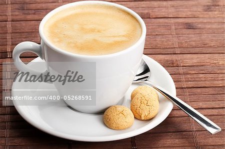 coffee in a white cup with amarettini and a spoon on wooden background