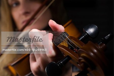 Young woman playing on violin on dark background