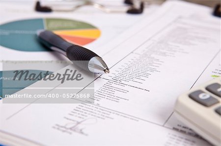 Report table with ballpoint pen on top, calculator and chart diagram in the background