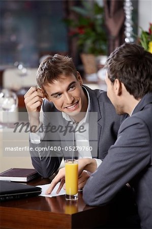 Two smiling business men have dinner at restaurant