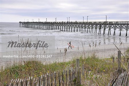 The fishing pier at Surf City, NC on Topsail Island just before dusk.  A surfer is carrying a surf board in the distance.