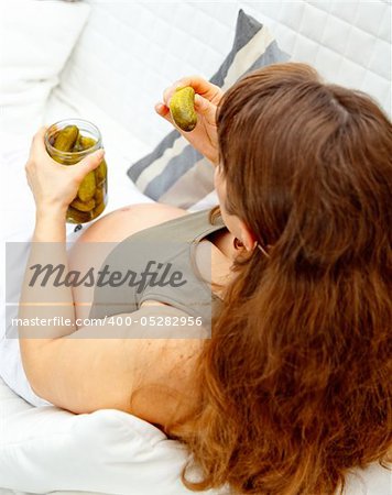 Pregnant woman sitting on sofa at home and  holding  jar of cucumbers in hands. Closeup.