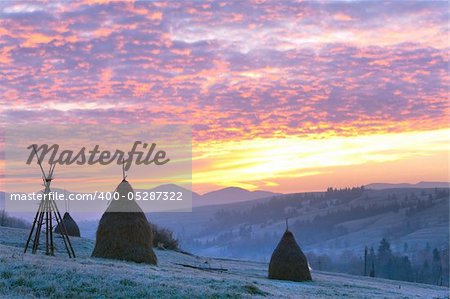 first autumn frosts on pasture with haystacks and majestic sunrise in the mountains village