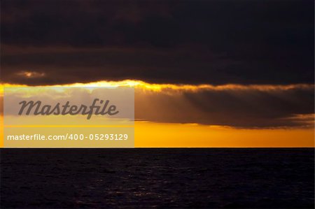 The sun rises behind storm clouds on the ocean