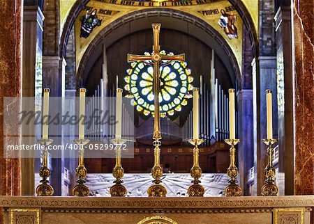 Set of ornate carved candlesticks on altar illuminated by sunlight with the brilliant window and organ pipes in the far background of the church