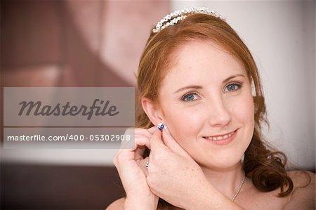 red head sexy beautiful bride inserting her earrings in whilst smiling