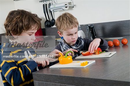 Two boys cutting some red and yellow peppers, used for cooking.