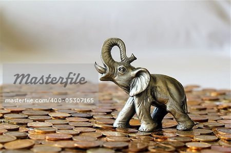 Horisontal composition of silver elephant sitting on the heap of coins .