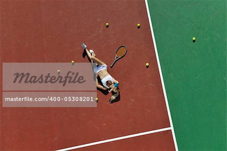 young fit woman playing tennis outdoor on orange tennis field at early morning