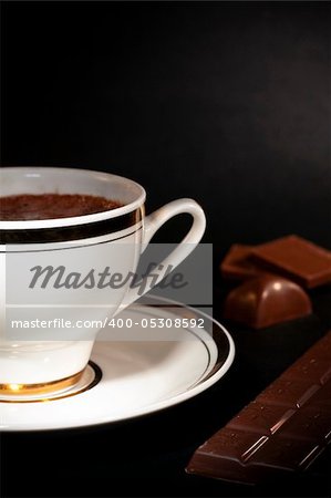 A white cup filled with hot luxury chocolate drink and chocolate bars on black background
