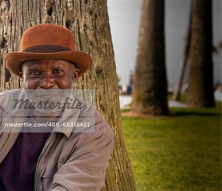 A happy man sitting on the beach.  There are trees in the background and some green grass.