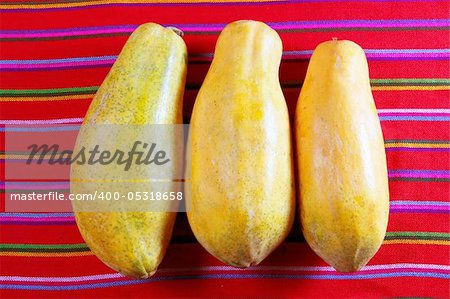 three papaya fruits on latin serape tablecloth  red background