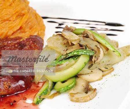 A pile of fried vegetables (zucchini, mushroom) with a piece of meat and mashed sweet potatoes in the background (Selective Focus, Focus on the pile of vegetables)