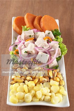 Peruvian-style ceviche made out of raw dogfish (Spanish: tollo), red onions and aji (Peruvian hot pepper) and served with corn, roasted corn (cancha) and cooked sweet potato (Selective Focus, Focus on the front of the fish)