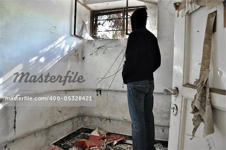 Hooded man looking through the broeken window of abandoned house.