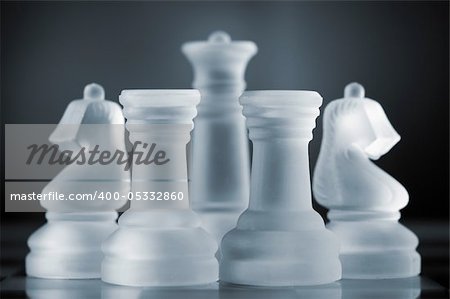 glass chess pieces are defending the queen on board in dark