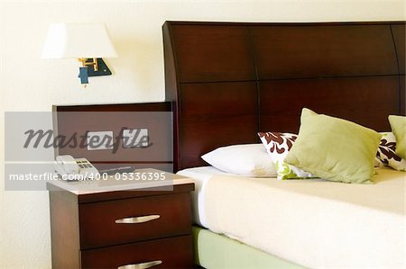 Hotel bed with green pillows and a telephone on cupboard.