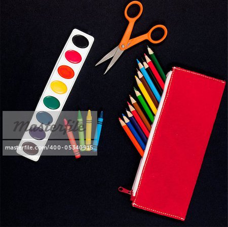 Art supplies for students starting school: colored pencils, paints, crayons, scissors on black background