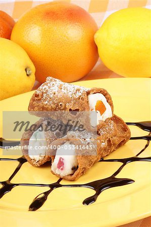 Close-up of original mini sicilian cannoli over a yellow plate. These tube-shaped pastries are made of fried shells filled with a sweet mixture of ricotta cheese, chocolate, candied fruit and sprinkled with icing sugar.