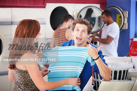 Unhappy man with girlfriend holds a shrunken t-shirt in laundromat