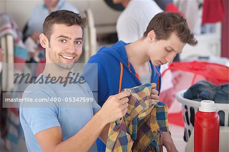 Smiling Caucasian man holds plaid shirt in laundromat