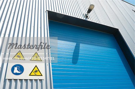 industrial unit with blue roller door and some warning signs