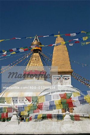 Boudhanath Stupa. Golden spire and all seeing Buddha eyes on top a giant white hemisphere. Smaller stupa in foreground. Kathmandu, Nepal