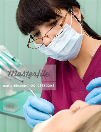 Female dentist with protection mask and gloves examining patient